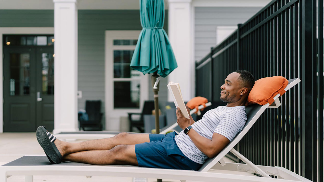 Man reading book on pool lawn chair