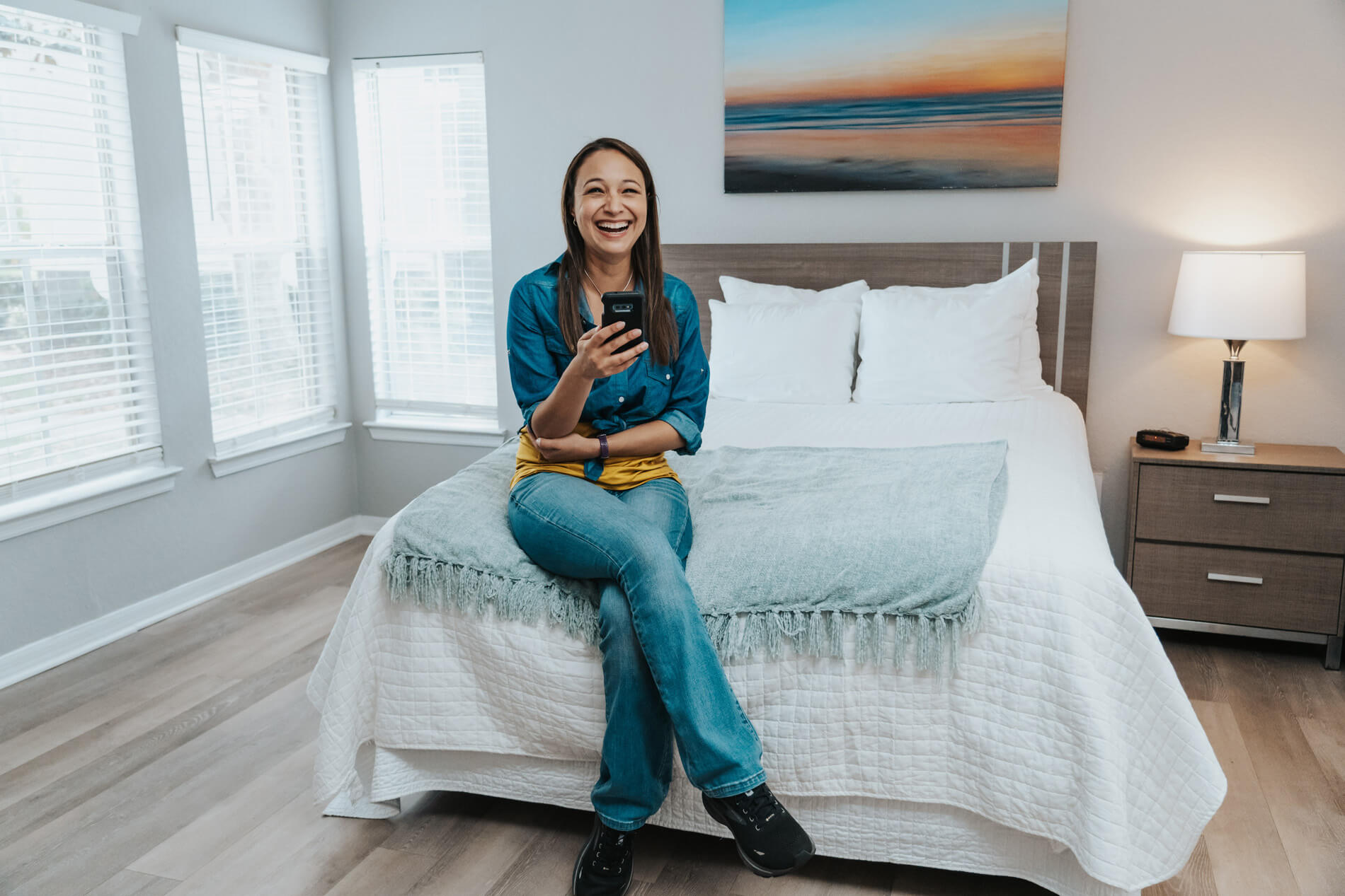 Arbors At Maitland woman plays on a phone in a staged bedroom